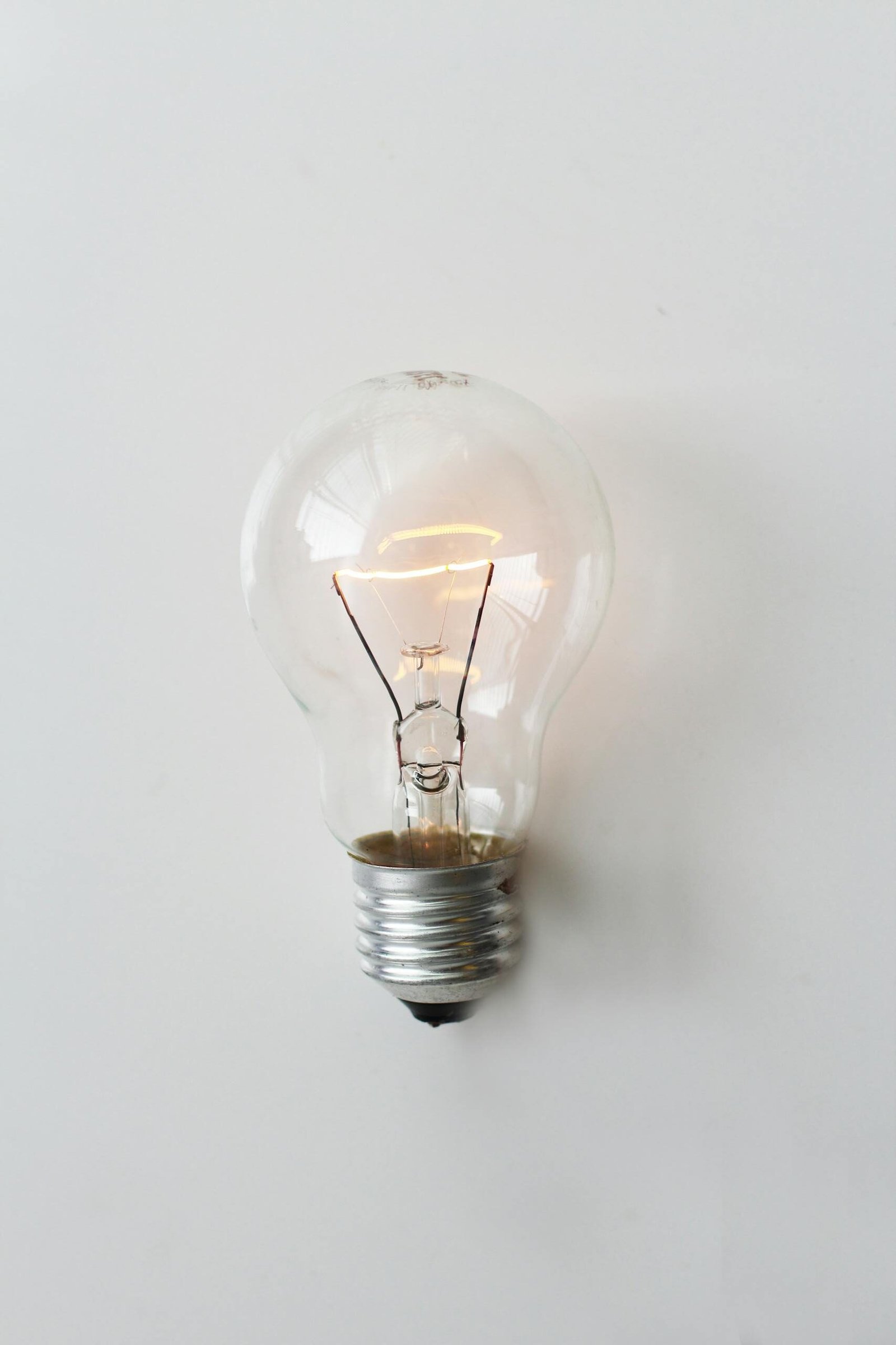 A close-up of an illuminated incandescent light bulb against a white background.